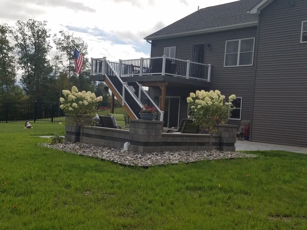 Raised deck and a stone patio area in the backyard by Sleek Scapes.