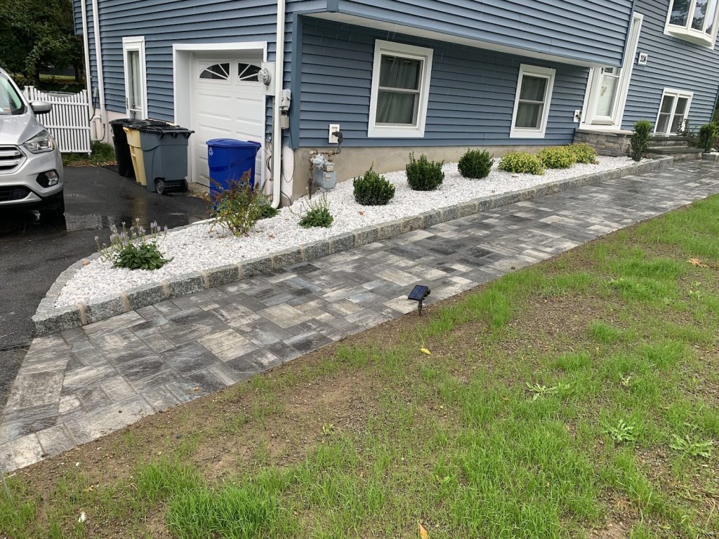 Gray paver walkway with stone borders and white gravel landscaping by Sleek Scapes.